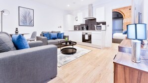 Un appartement moderne avec un canapé gris, une table basse, un coin cuisine et un salon doté d’une grande fenêtre.