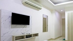 A room with a mounted TV, an air conditioner, and a door. - Hotel Lee Benz (New Delhi)