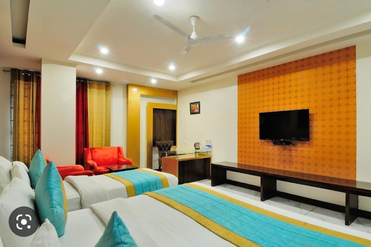A hotel room with two beds, a desk, a TV, and a ceiling fan.