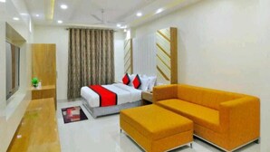 A modern hotel room with a bed, a sofa, a desk, and a ceiling fan. - Hotel Lee Benz (New Delhi)