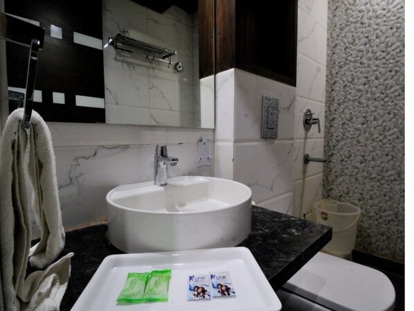A bathroom with a white sink, a mirror, and a toilet. There are two green packets on the sink.