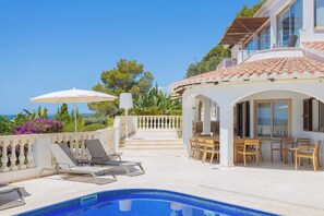 A poolside area with lounge chairs, a dining table, and umbrellas. - Villa Treya - Star property, stunning views (San Jaime Mediterráneo)