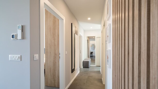 A modern hallway with a wooden door, a grey bench, and a wall-mounted light fixture.
