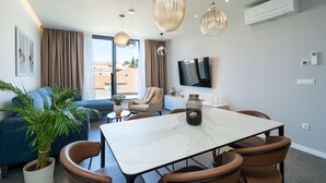 A modern living room with a sofa, a dining table with chairs, a TV, and a large window with curtains.