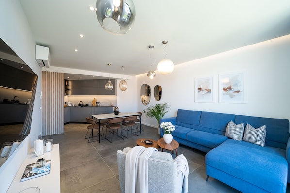 Una sala de estar moderna con un sofá azul, una zona de comedor y una cocina al fondo.