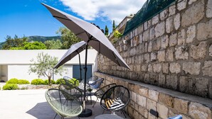 An outdoor seating area with chairs and tables, a large umbrella, and a stone wall.