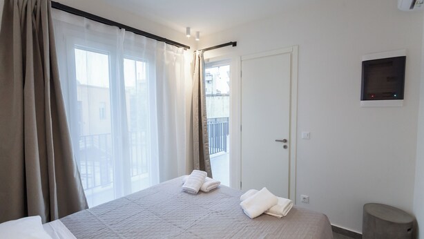 Ett hotellrum med en säng, ett fönster med gardiner, en dörr och en liten apparat som är monterad på väggen.