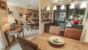 Ein Essbereich mit Holztisch und Stühlen, einer Obstschale und einer Küche im Hintergrund.