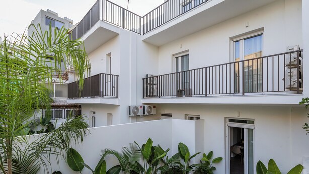 Een meerlaags woongebouw met balkons, airconditioning en weelderige beplanting.