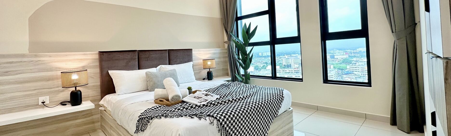 A modern hotel room with a large bed, two bedside lamps, a view of the city, and a large window.