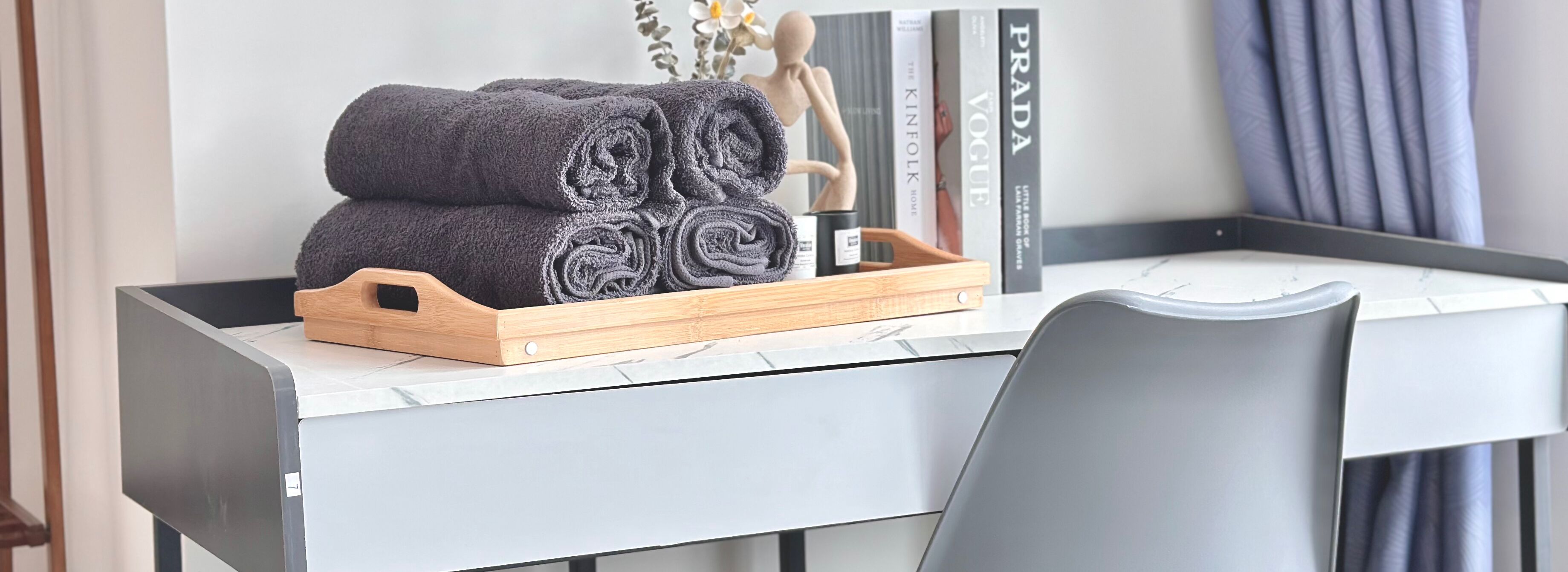 A neatly arranged workspace with a wooden tray holding rolled towels, a mannequin, and books on a marble desk.