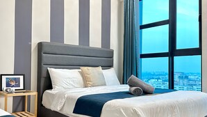 A neatly made bed with white and blue bedding, a grey headboard, and a city view through large windows. - Ong Kim Wee Residence (Malacca City)