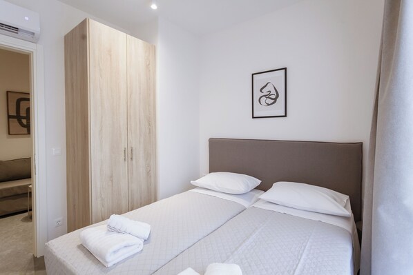 A neatly made bed with white linens and pillows, a wooden wardrobe, and a framed abstract artwork on the wall.