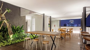A rooftop terrace with a wooden table and chairs, surrounded by greenery and overlooking a cityscape at night. - Sakura Terrace Benhil (Jakarta)