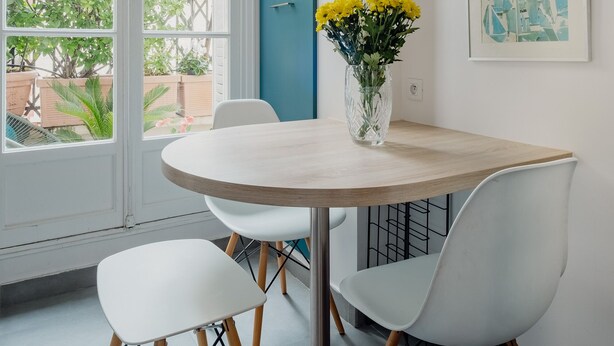 A modern dining area with a round table, white chairs, and a vase of yellow flowers. - Wanderer's Retreat, by Veeve (Paris)