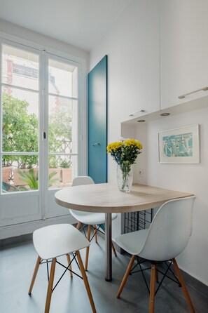 A modern dining area with a round table, white chairs, and a vase of yellow flowers. - Wanderer's Retreat, by Veeve (Paris)