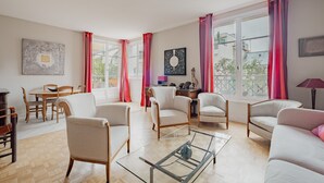 A spacious living room with a wooden floor, a glass coffee table, and multiple seating options including a sofa and armchairs. - Wanderer's Retreat, by Veeve (Paris)