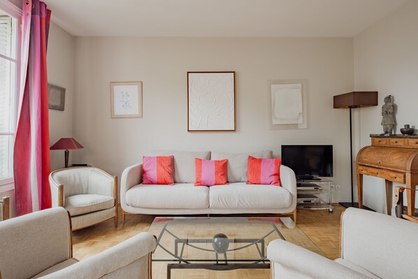 A living room with a white sofa, two armchairs, a glass coffee table, and a TV. - Wanderer's Retreat, by Veeve (Paris)