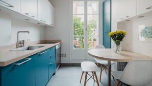 A modern kitchen with a built-in dishwasher, a sink, and a dining area with a table and chairs. - Wanderer's Retreat, by Veeve (Paris)