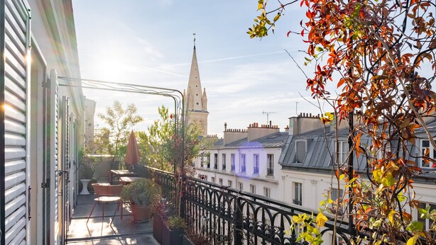A balcony with outdoor seating, potted plants, and a view of a church tower. - Spire View, by Veeve (Paris)