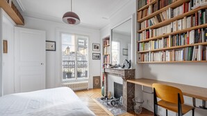 A bedroom with a large bed, a wooden desk, a bookshelf, and a fireplace. - Spire View, by Veeve (Paris)