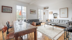 A spacious living room with a wooden dining table, grey sofas, and a white rug. - Spire View, by Veeve (Paris)