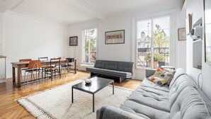 A spacious living room with a grey sofa, a dining table with chairs, and a white rug. - Spire View, by Veeve (Paris)