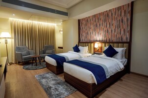 Habitación de hotel con dos camas, un sofá, un escritorio y un amplio mural abstracto en la pared.