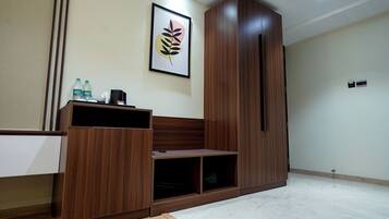 A room with a wooden wardrobe, a framed artwork on the wall, and a shelf with water bottles.