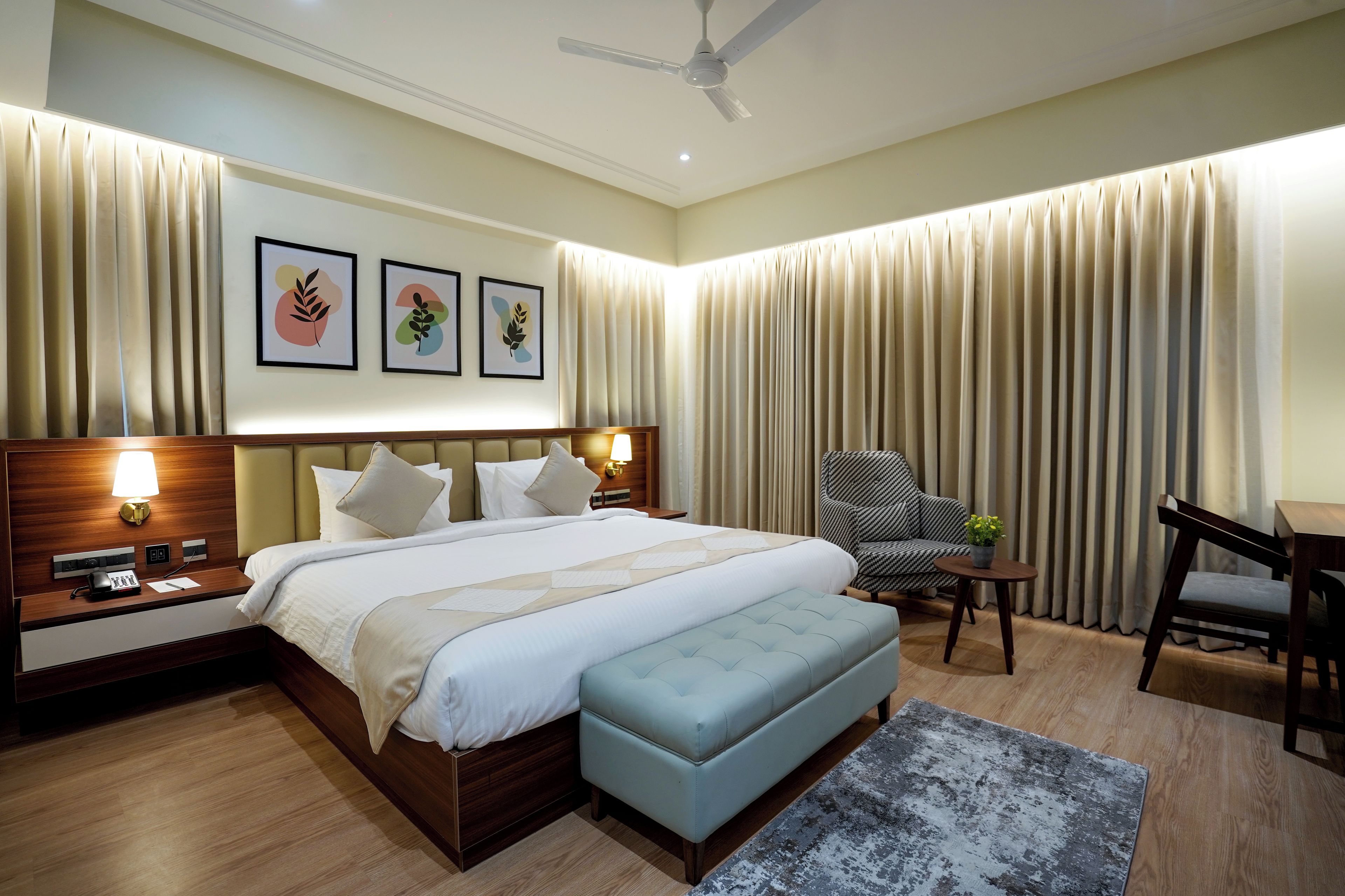 A hotel room with a bed, bedside tables, a desk, a chair, and a ceiling fan.