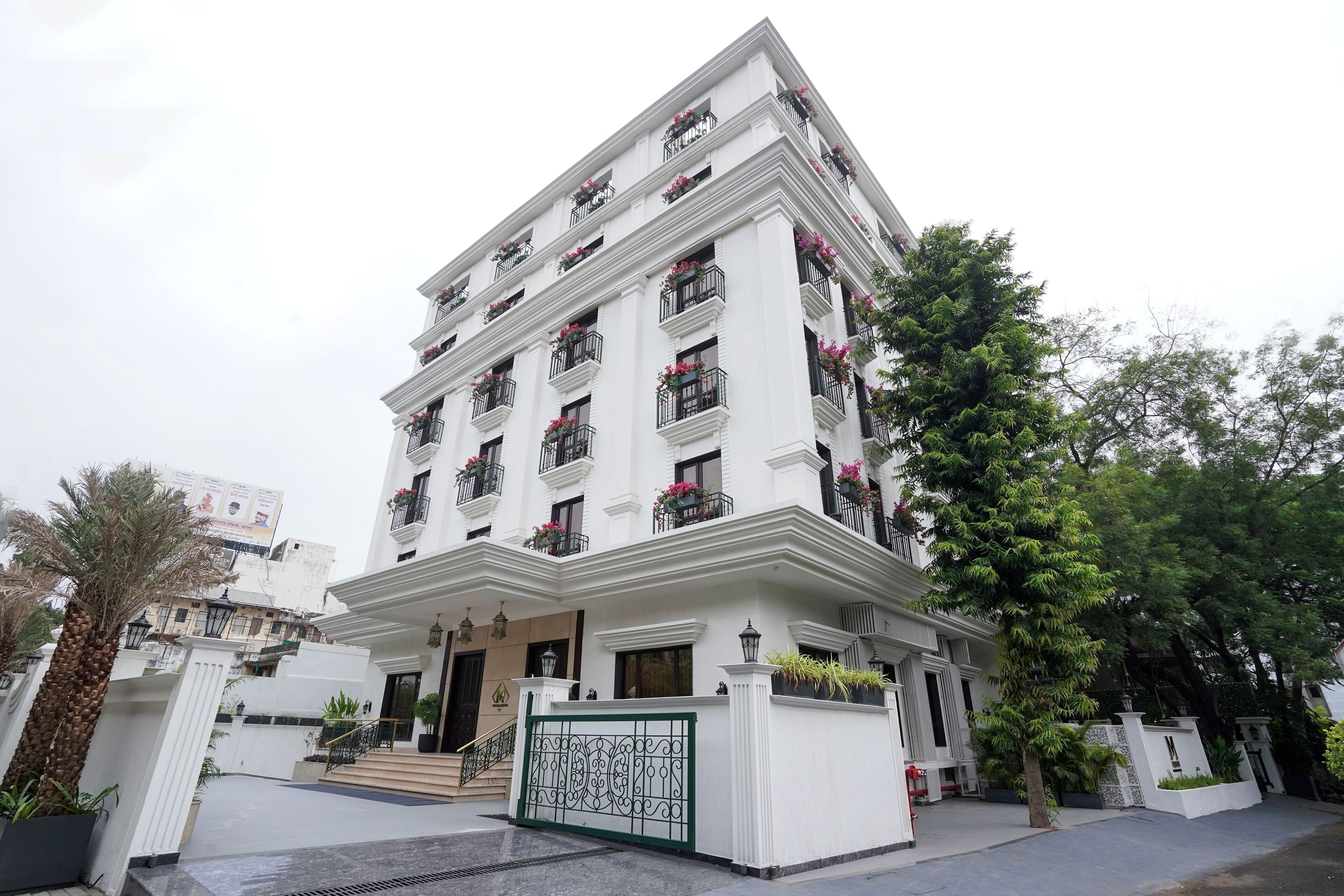 A multi-story building with balconies, a gated entrance, and surrounding greenery.
