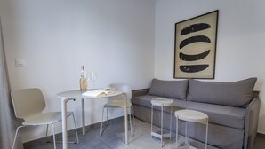 Un salon moderne avec un canapé gris, deux fauteuils blancs, une petite table ronde et une haute table d’appoint blanche.