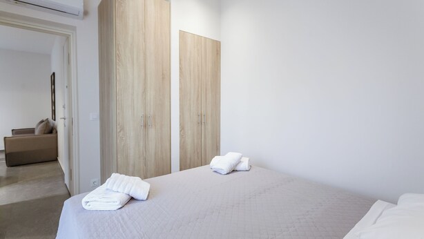 Une chambre d’hôtel moderne avec un grand lit, une armoire en bois et un petit coin salon.