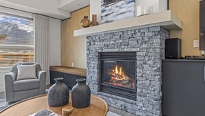 Ein modernes Wohnzimmer mit Kamin aus Stein, einem grauen Sofa und einem Couchtisch mit Vasen.