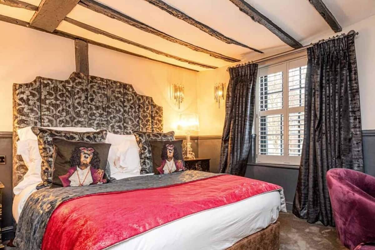 Quarto com uma cama grande, cabeceira com design estampado, janela com cortinas e um cobertor vermelho.