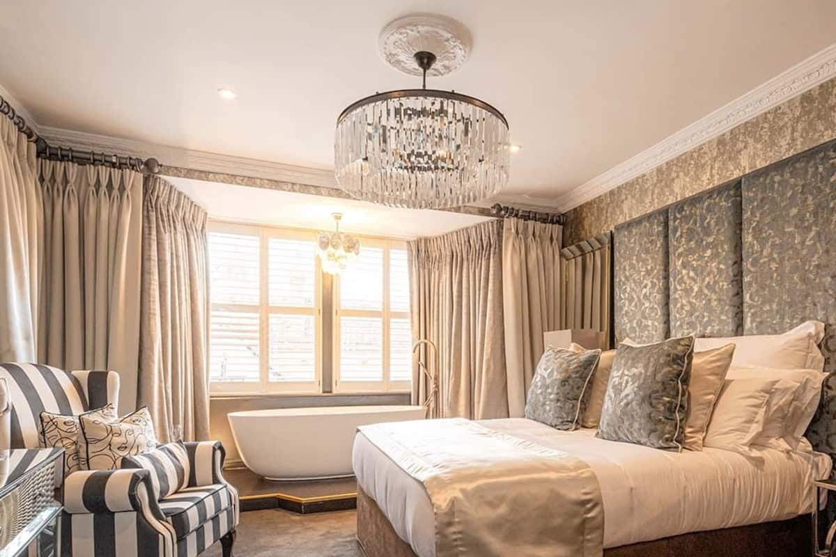 Quarto com cama grande, chaise longue, banheira e lustre.