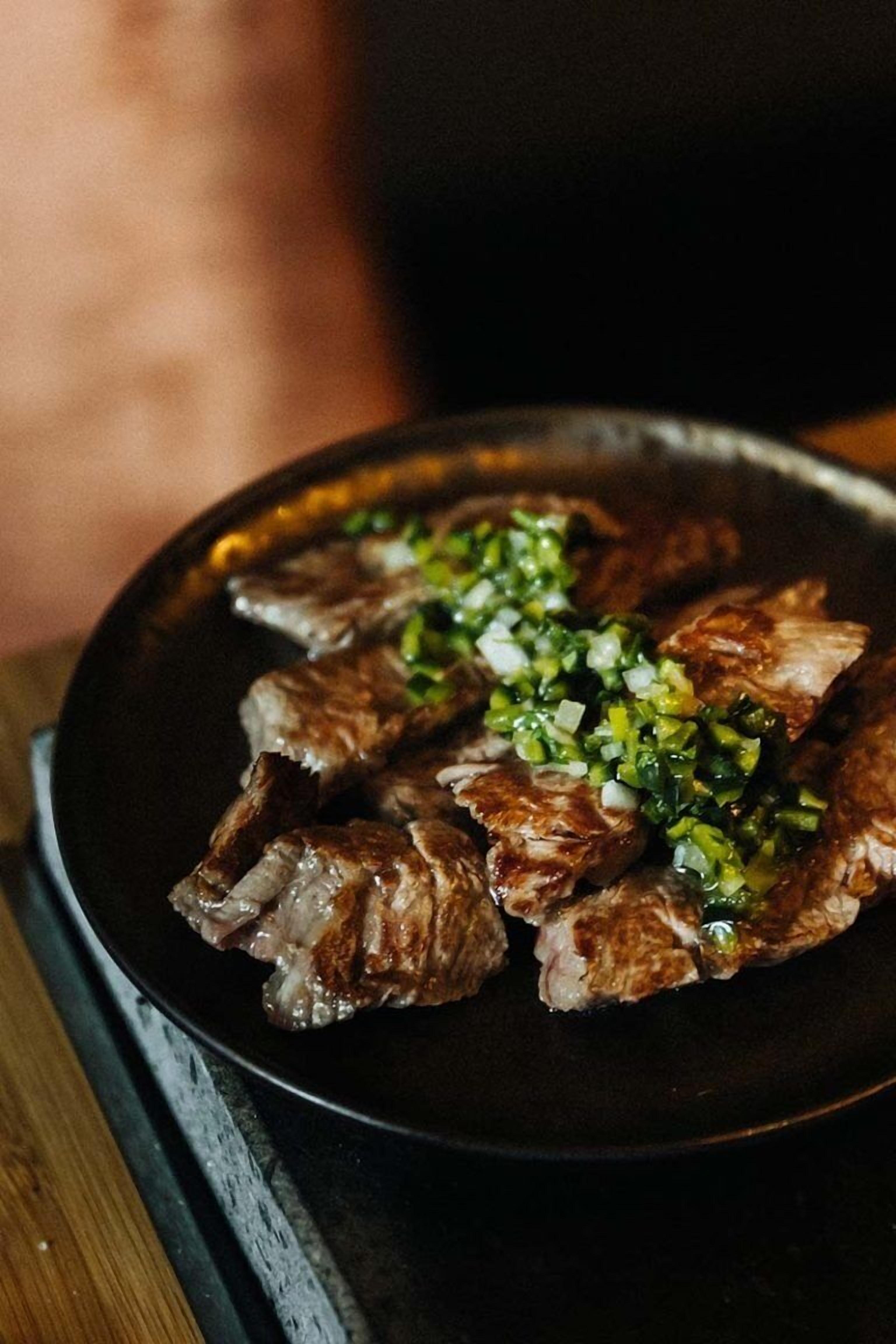 Un plato de carne a la parrilla con hierbas verdes picadas.