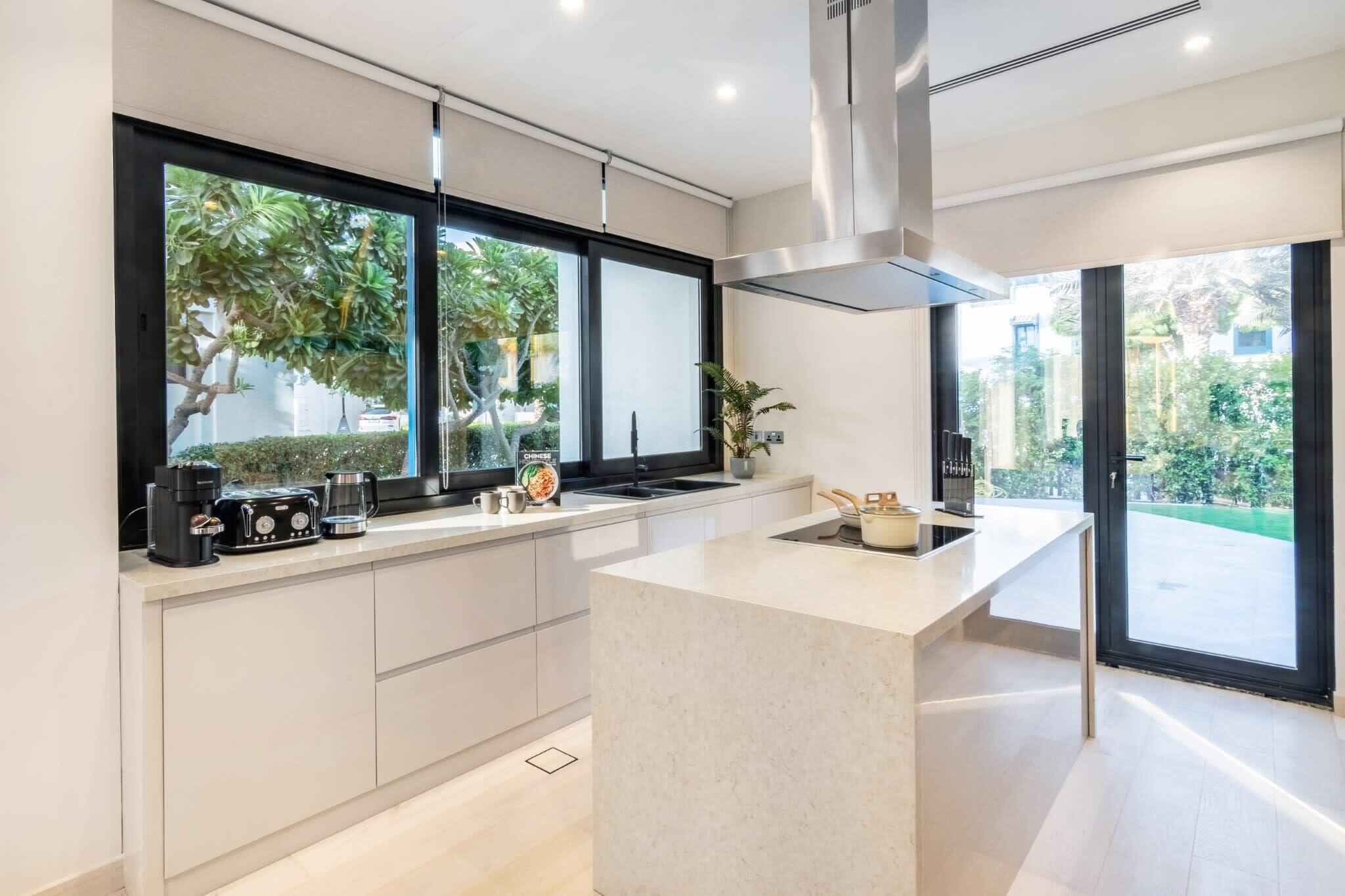 Een moderne keuken met een groot kookeiland, inbouwapparatuur en grote ramen met uitzicht op groen.