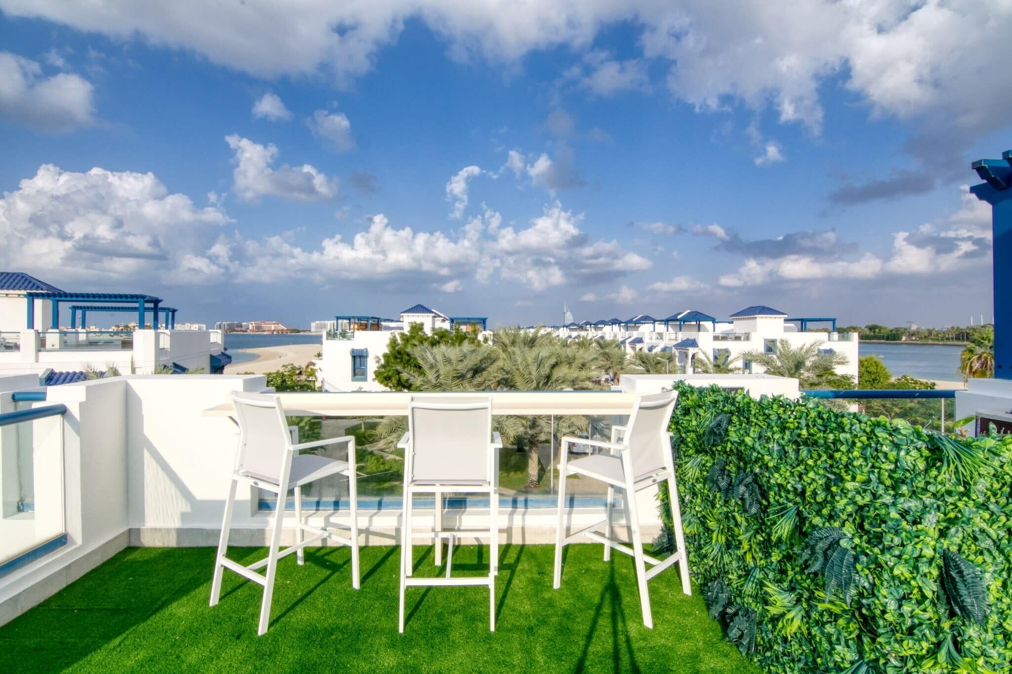 A rooftop terrace with a dining table and chairs, surrounded by lush greenery and a view of the sea.