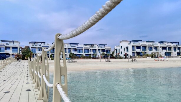 A wooden promenade leading to a beach with modern buildings in the background.