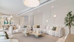 A modern living room with two white sofas, a coffee table, and a dining area with chairs.
