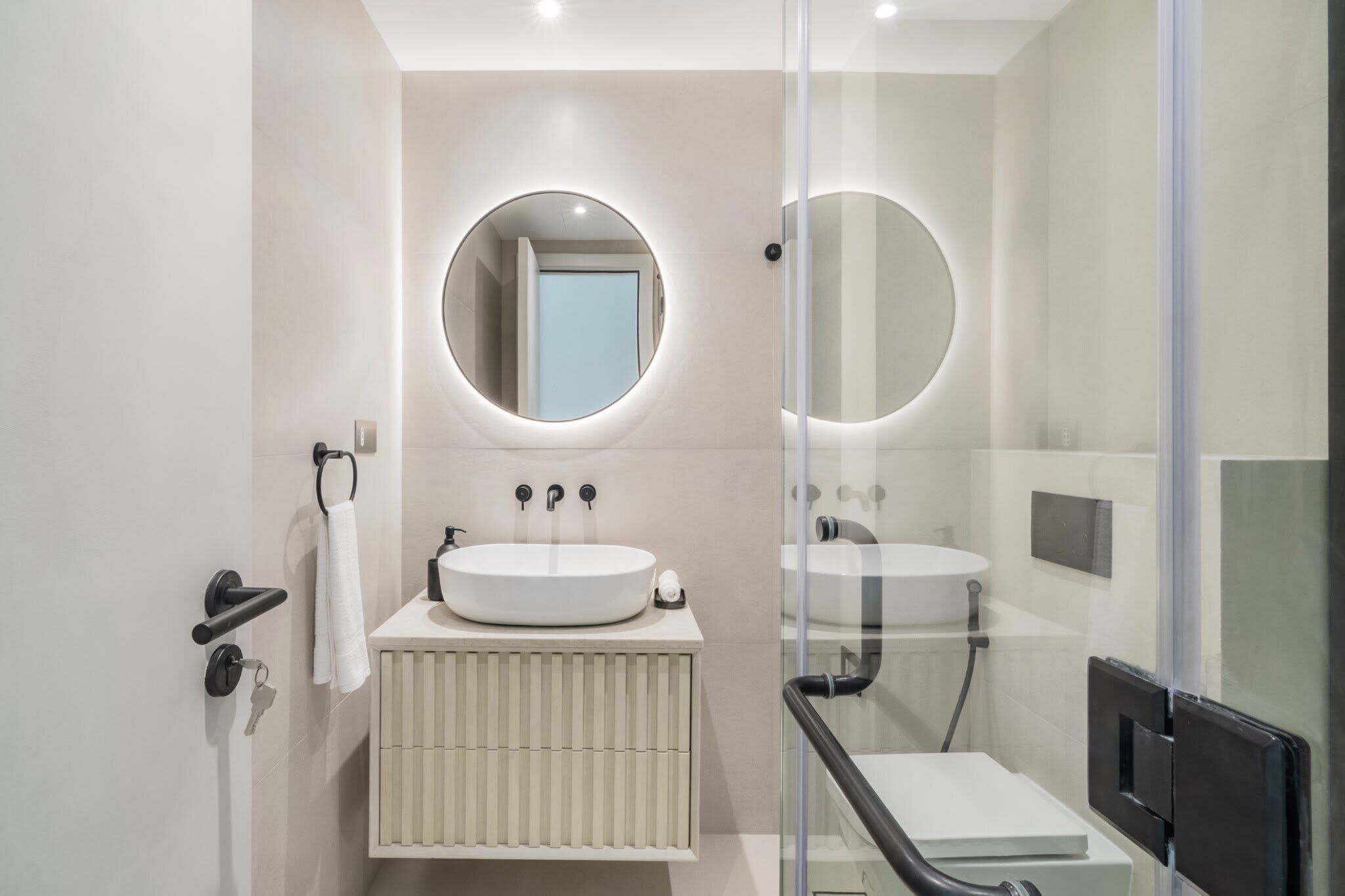Un baño moderno con un espejo redondo, dos lavamanos y un inodoro.