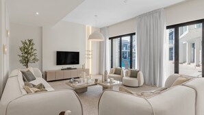 A modern living room with a flat-screen TV, two sofas, a coffee table, and a large window with a view of a pool and building.