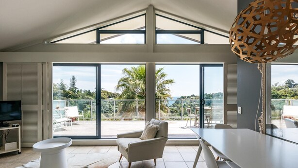 A modern living room with a large glass door leading to a balcony, a dining area with a table and chairs, and a television on a stand.