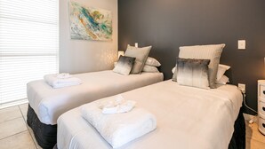 A hotel room with two beds, each with white linens and towels, a dark accent wall, and a piece of abstract art.