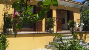 Un edificio amarillo con entrada de baldosas, plantas en macetas y una escalera que lleva a la puerta.