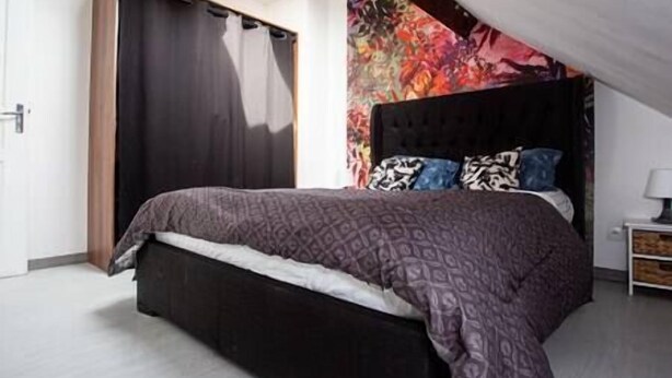 A bedroom with a bed, a wardrobe, and a colorful tapestry on the wall.