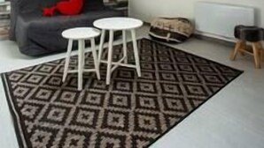 A loft-style room with a sloped ceiling, a stone-patterned wall, a black sofa with a red pillow, a patterned rug, and a small white table.