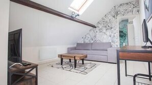 Ein Wohnzimmer mit hoher Decke, einem Sofa, einem Couchtisch, einem Fernseher und einem Gemälde an der Wand.