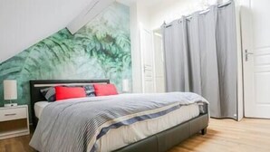 Ein Schlafzimmer mit einem Bett, einem Nachttisch, einer Lampe und einem großen Fenster mit Vorhängen.